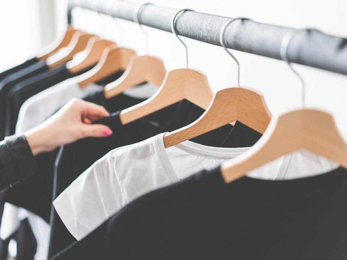 A customer browses black and white t-shirts hanging on steel retail rack.