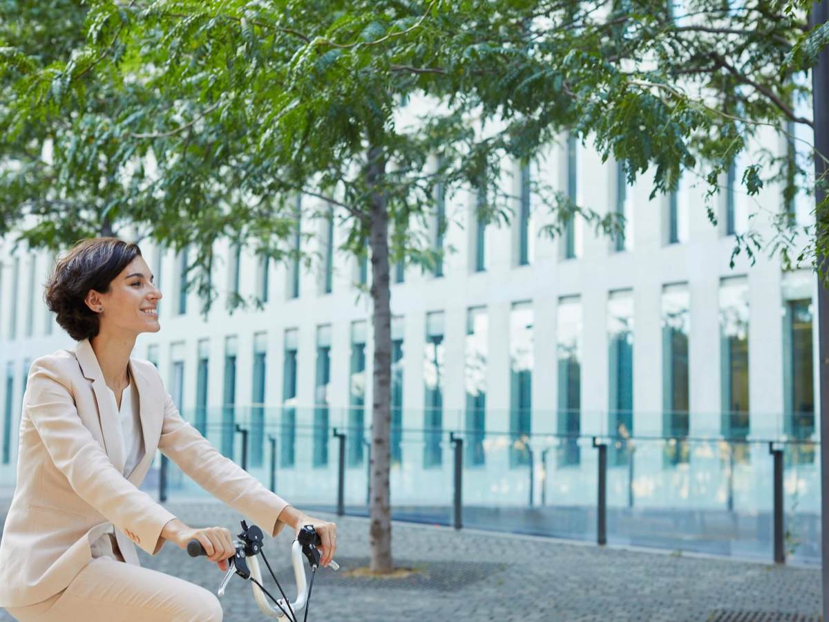 A happy business woman rides a bicycle through a city landscape
