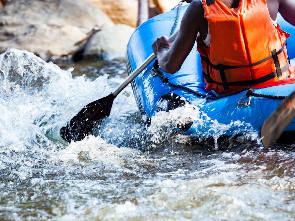 Blue raft in whitewaters with a person wearing an orange life jacket.