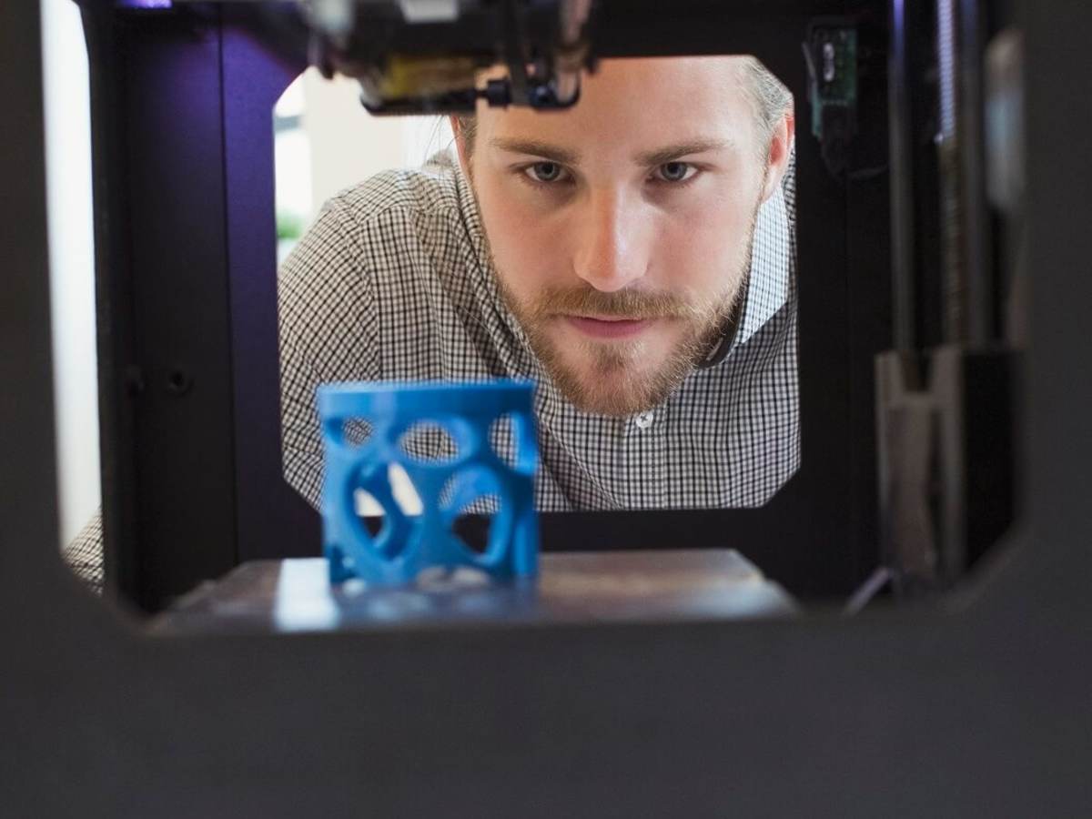 Man looks at a blue gadget made with additive manufacturing