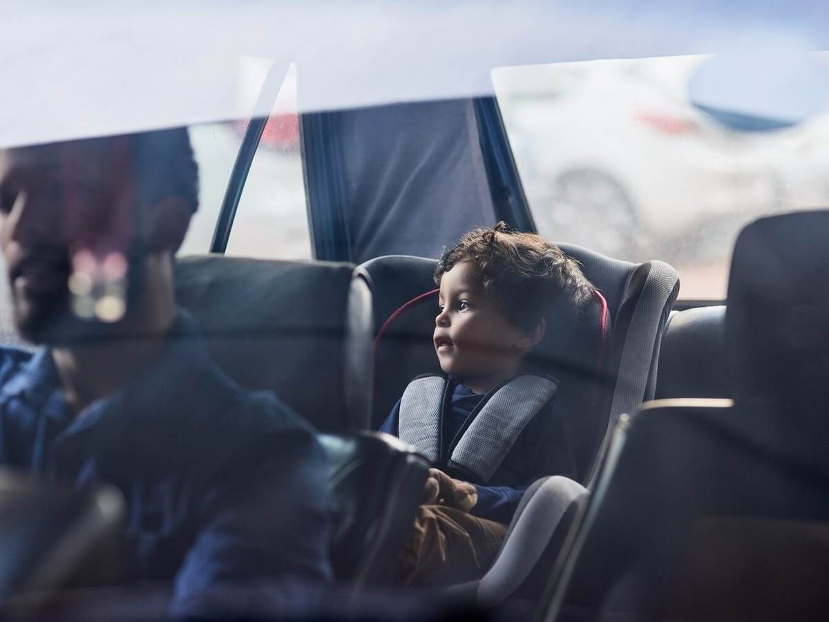 Parent driving with a toddler safely placed in the car's backseat.