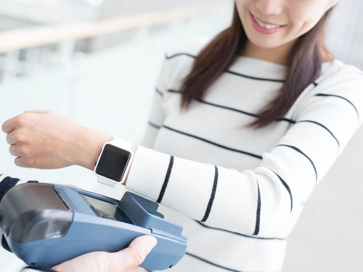 A woman holds her smartwatch up to a grey scanner
