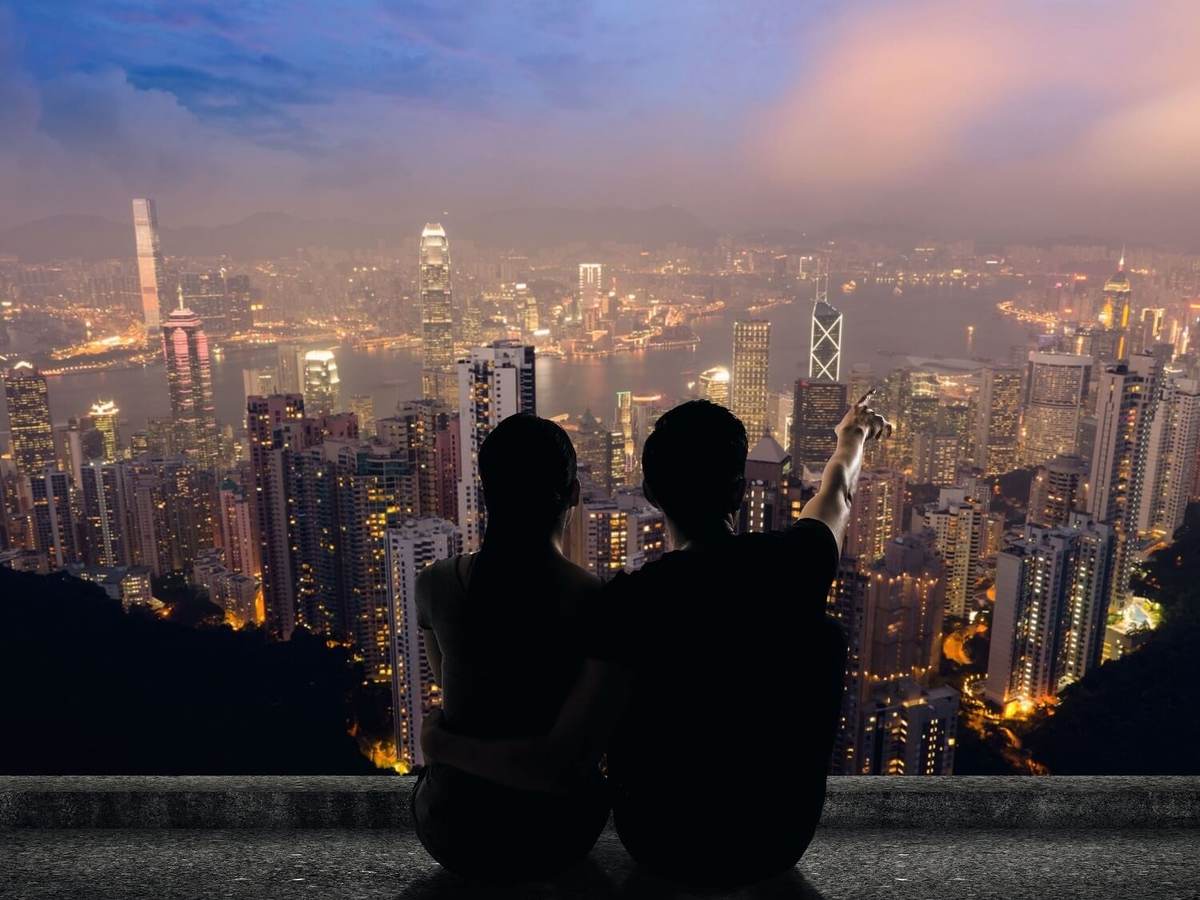 Silhouette of couple sit on ground point faraway on the roof above the city in the night.