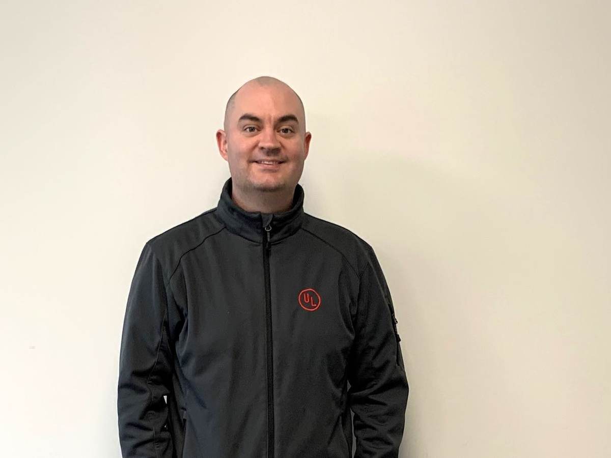 Seán Flannagan poses for EWeek picture. He's wearing a dark grey jacket with the red UL logo on its left pocket.