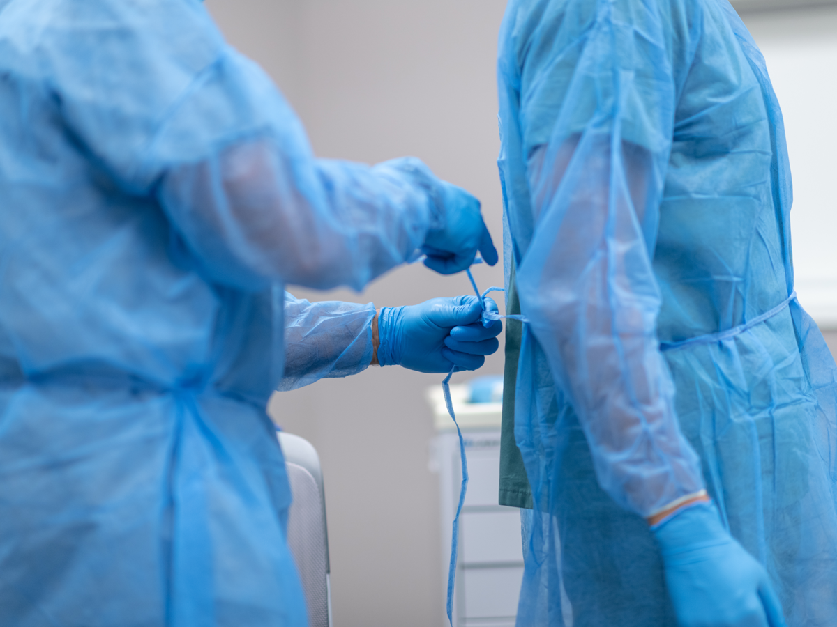 Medical worker ties a blue medical gown onto another worker.