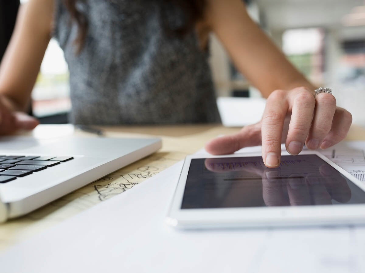 Close up of female architect at laptop using digital tablet in office