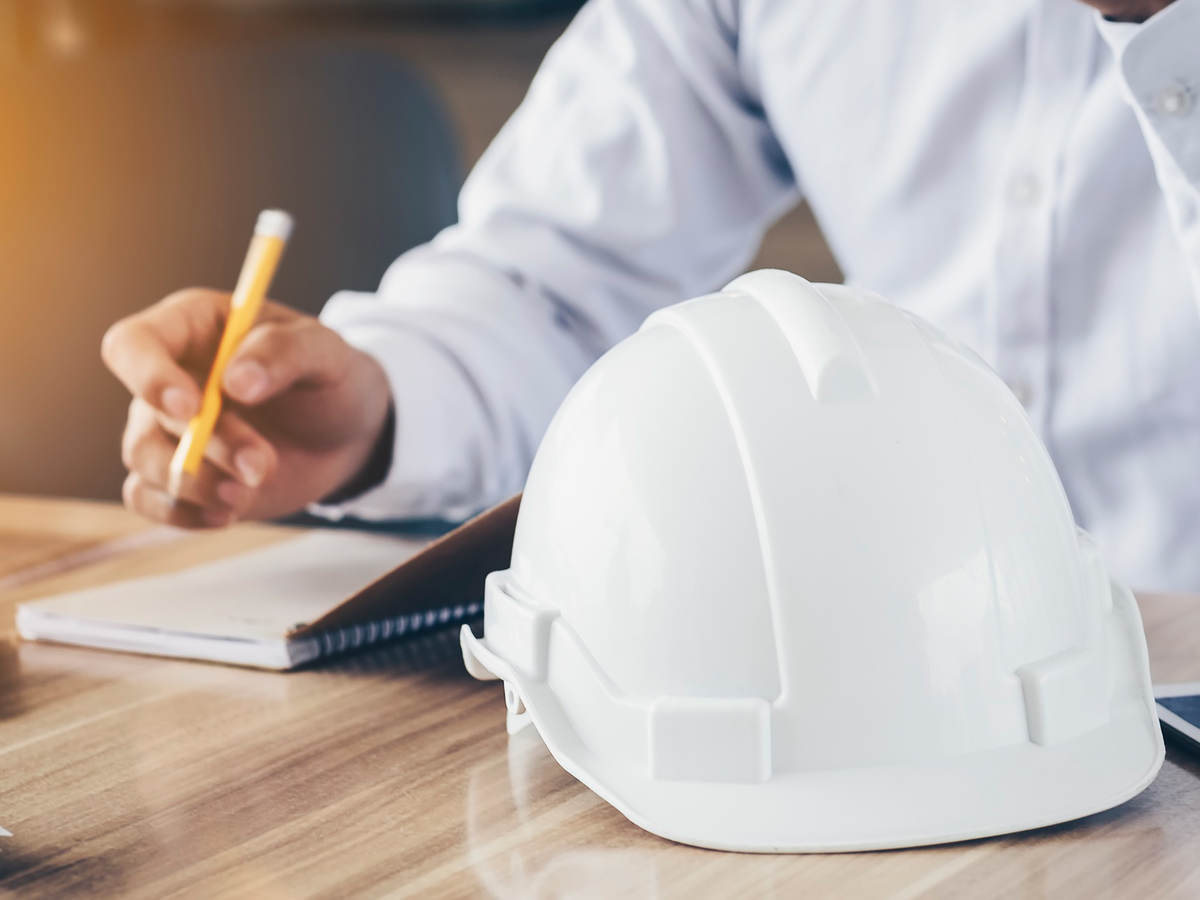 Photo of a person making notes, hard hat in foreground