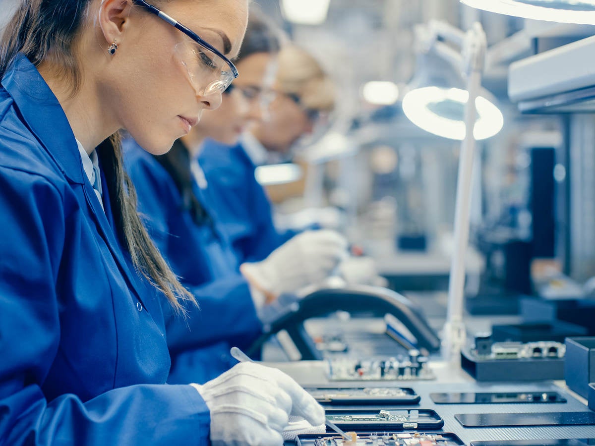 Female electronics factory workers in protective glasses assembling printed circuit boards 