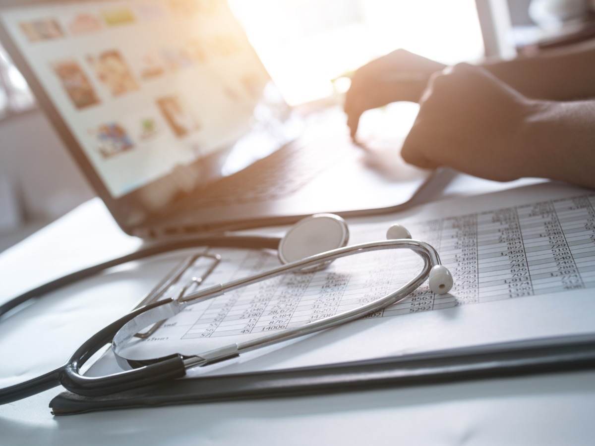Laptop on table beside stethoscope and medical chart