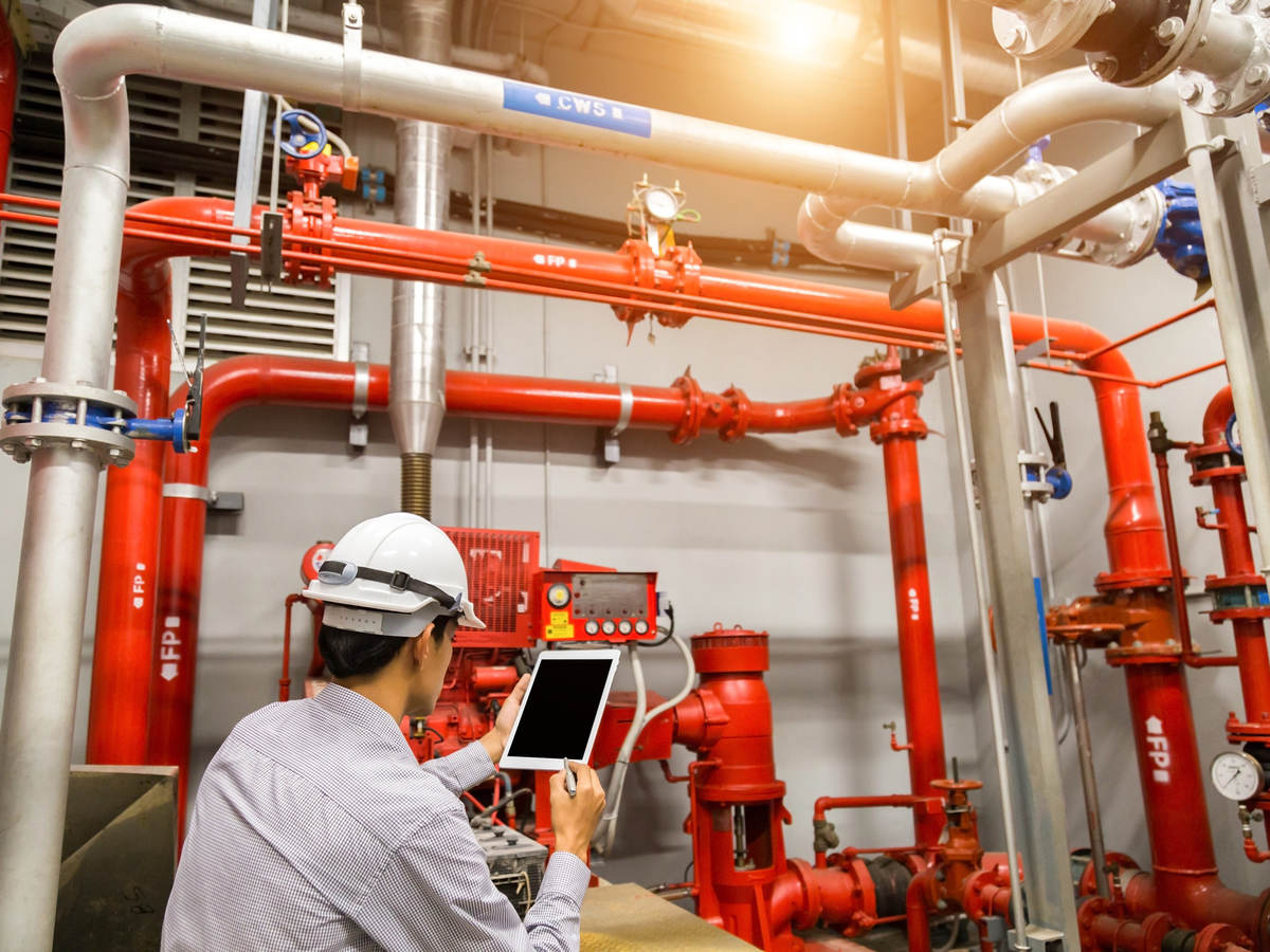 Engineer with tablet checks red generator pump for water sprinkler piping and fire alarm control system.