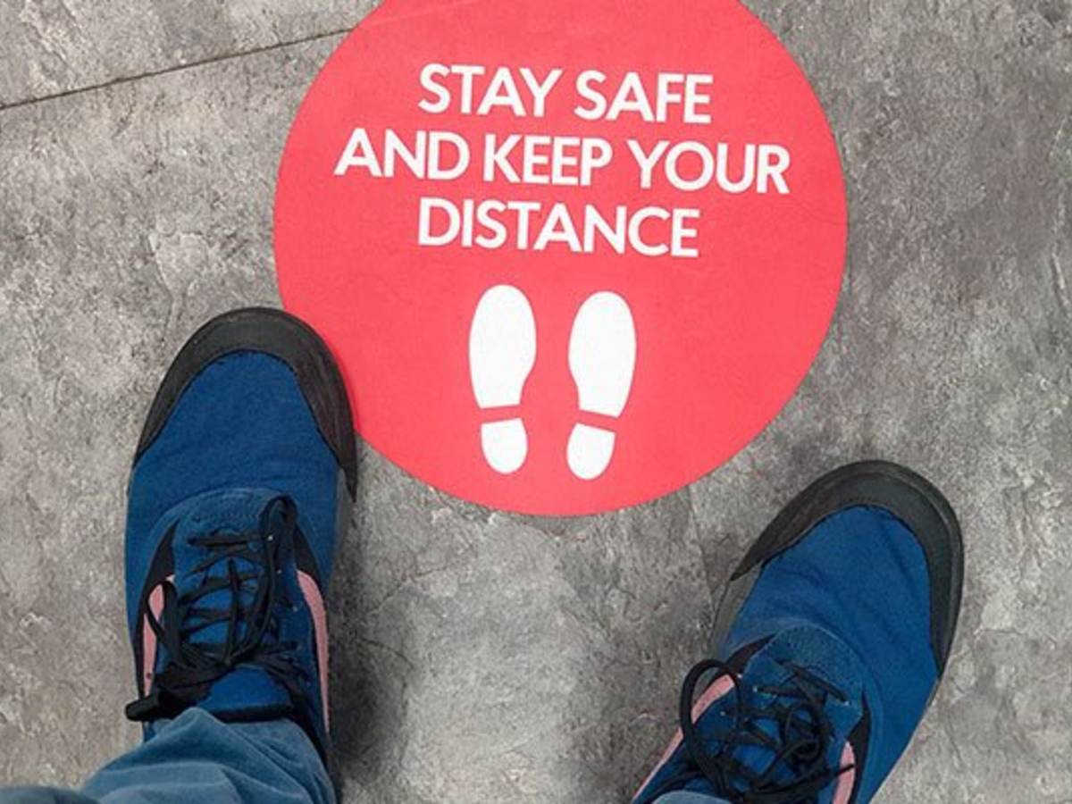 Two feet stand in front of a floor graphic that says stay safe and keep your distance