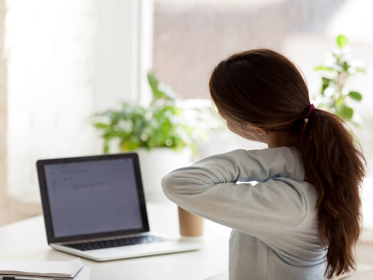 Back view of tired woman touching neck at work desk