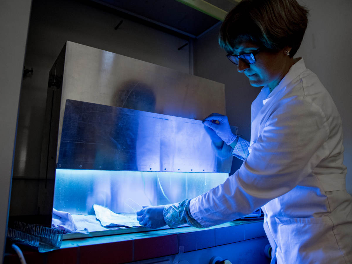 A woman uses UV light to inactivate harmful material on products.