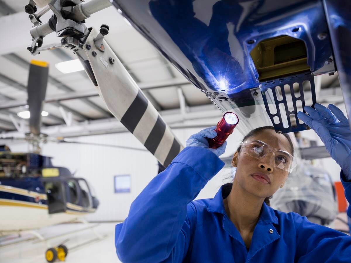 Female helicopter mechanic examining part with flashlight