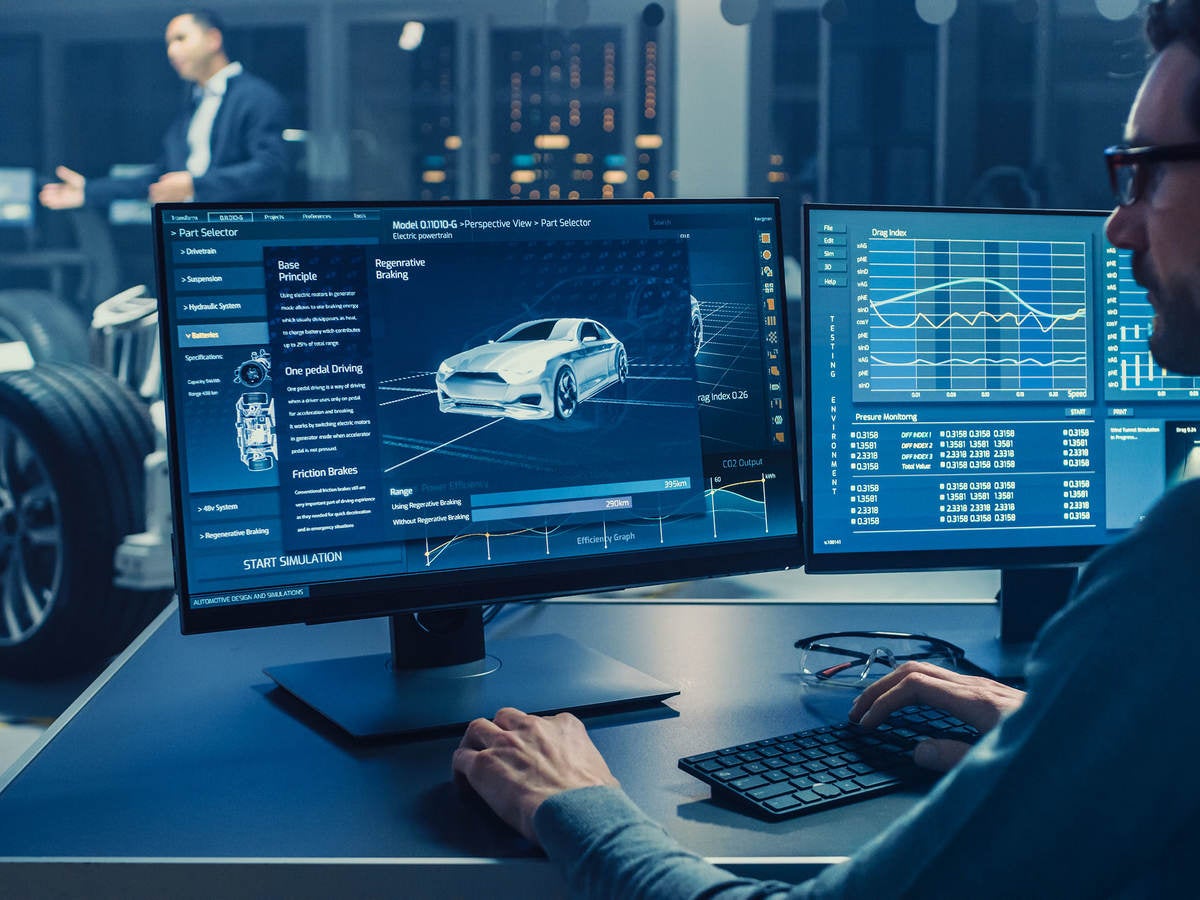Automotive engineer looking at a computer displaying a 3D electric car chassis prototype with wheels.