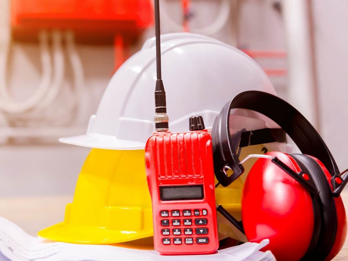 Construction hat, walkie talkie and earphones sitting on building plans