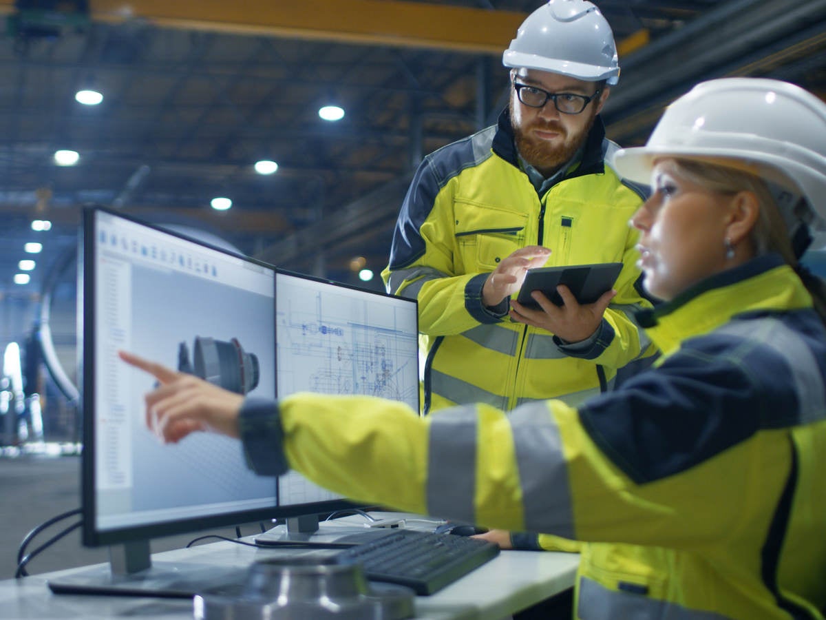 hard-hat wearing woman points to computer as man watches