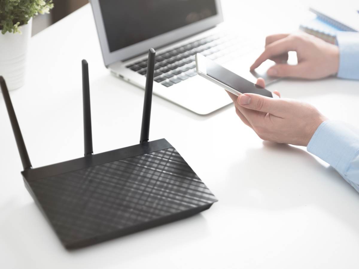 Wireless router positioned next to a laptop and mobile phone on a white table.