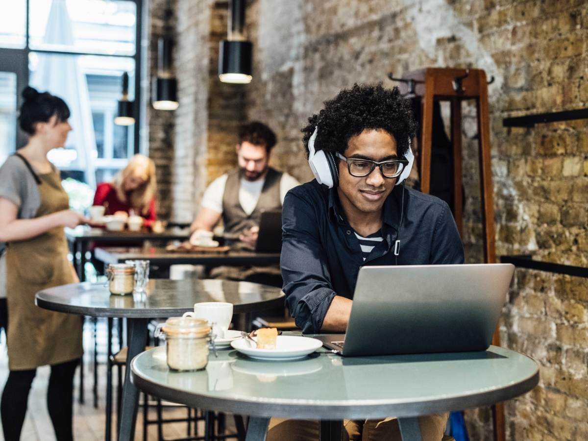 Man working on a computer wearing headphones in a cafe