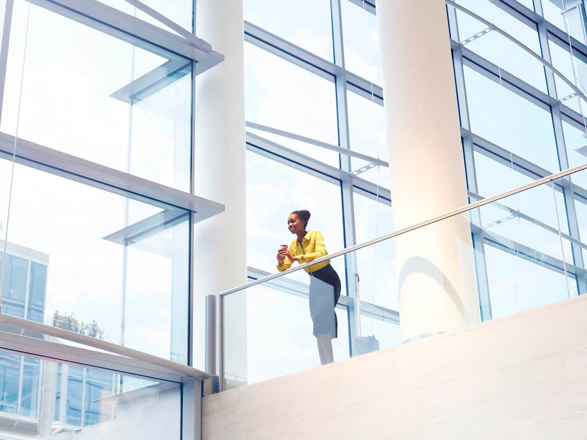 A Black woman looks down from the second floor of an interior office building.
