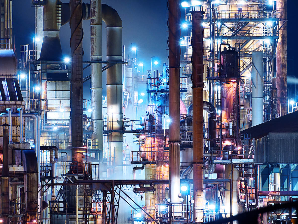 A brightly lit commercial oil refinery is shown at night.