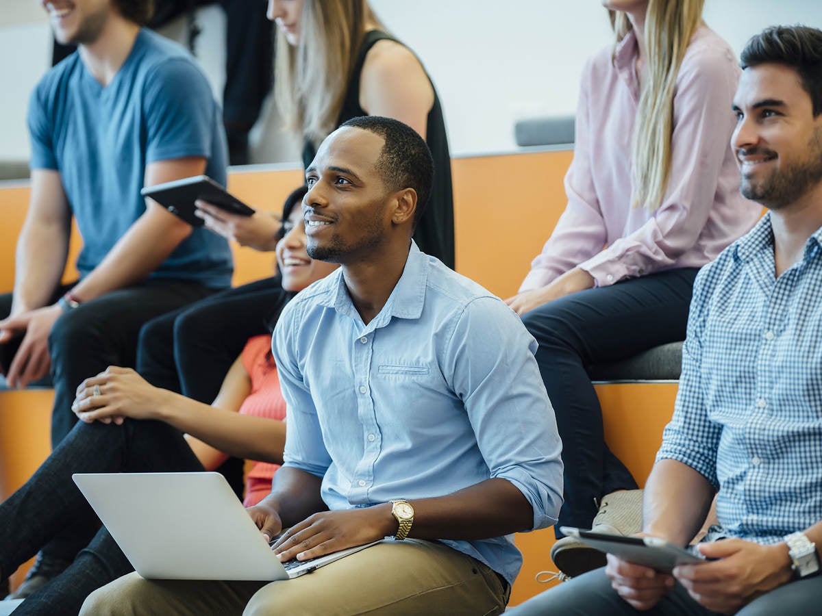 Group of people smiling with laptops while sitting in auditorium