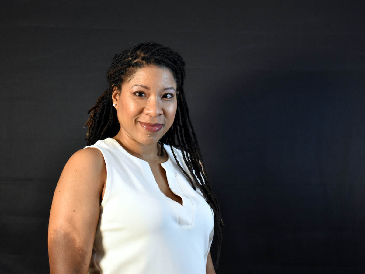 LaTanya Schwalb poses confidently wearing a white sweater while standing in front of a dark background.