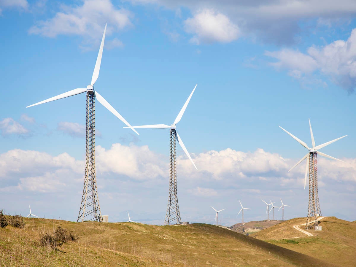 Wind turbines on a treeless hill under a blue sky with billowy clouds