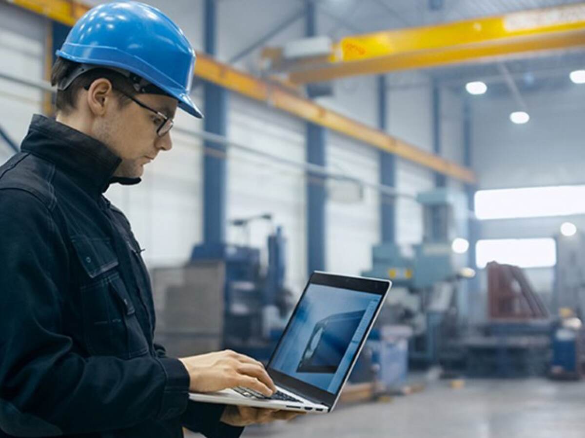 Factory worker in a hard hat using a laptop with engineering software