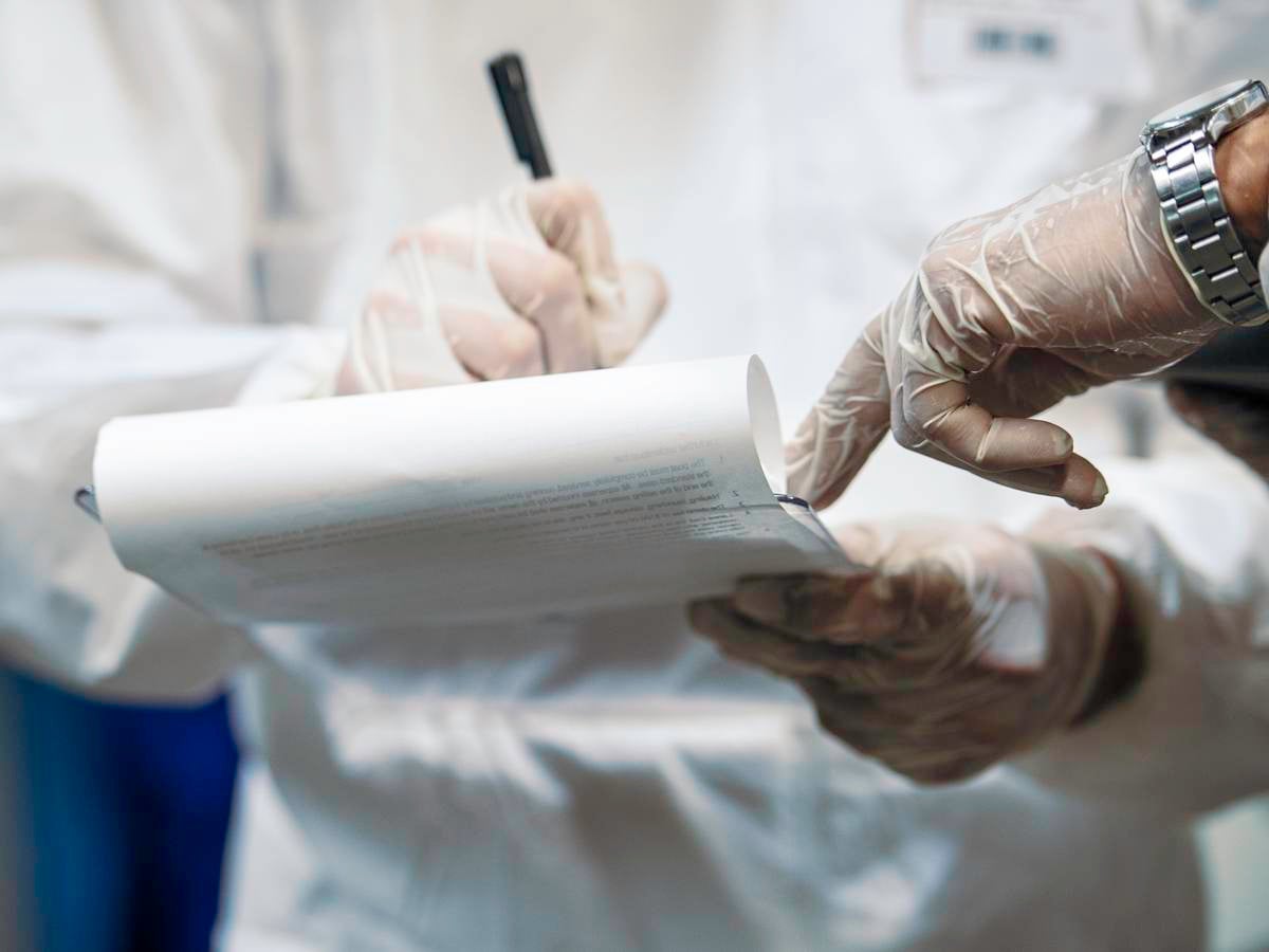 Two medical professionals' hands jotting down information on legal pad