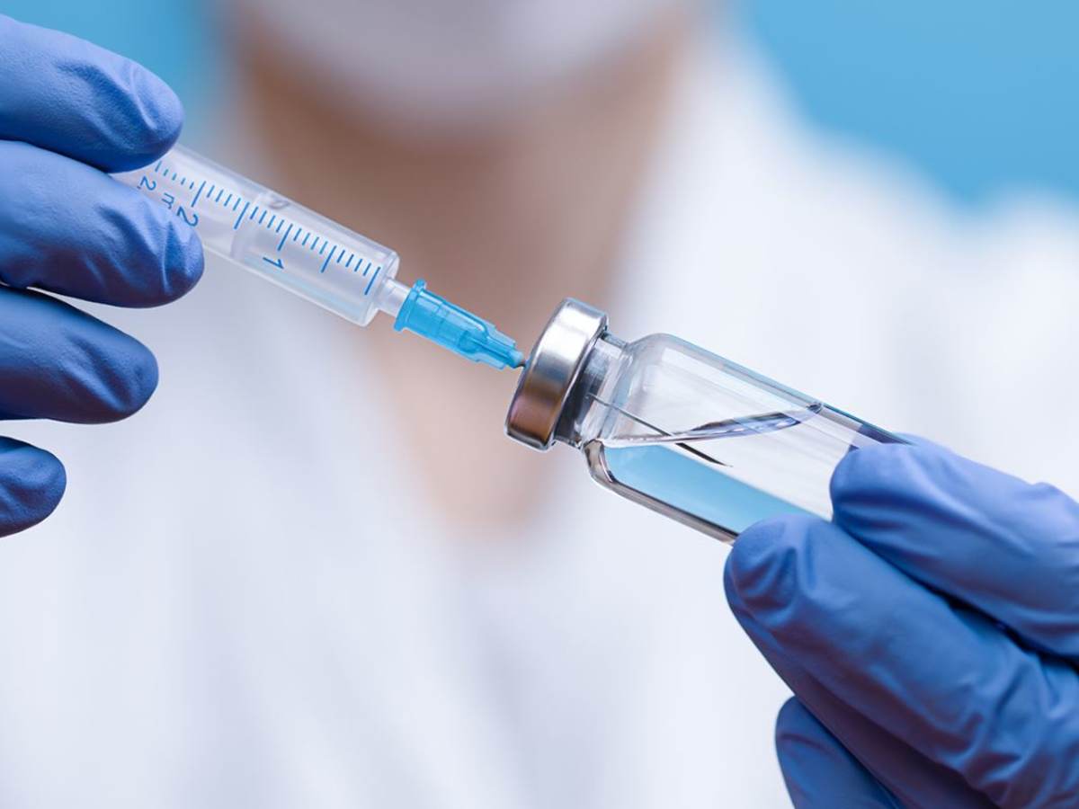 Healthcare worker wearing blue latex gloves hold syringe and vial of drug