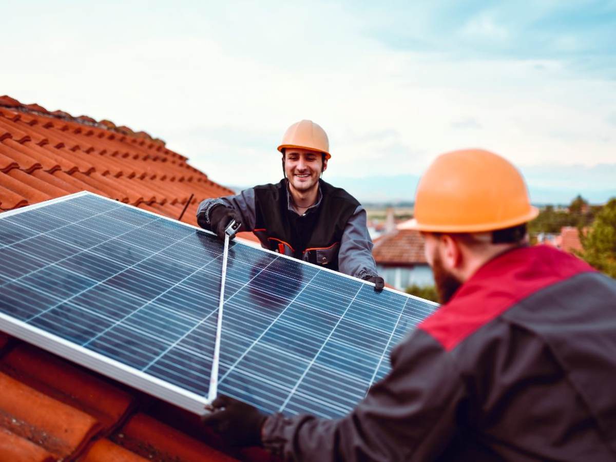 Two technicians install a solar planel on a tile rooftop