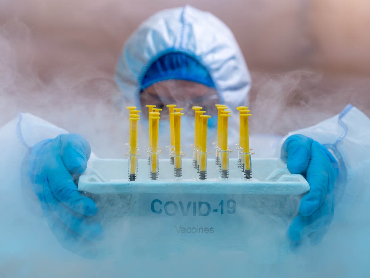 Medical worker with gloved hands inside a cold chamber holding a tray of COVID vaccines 