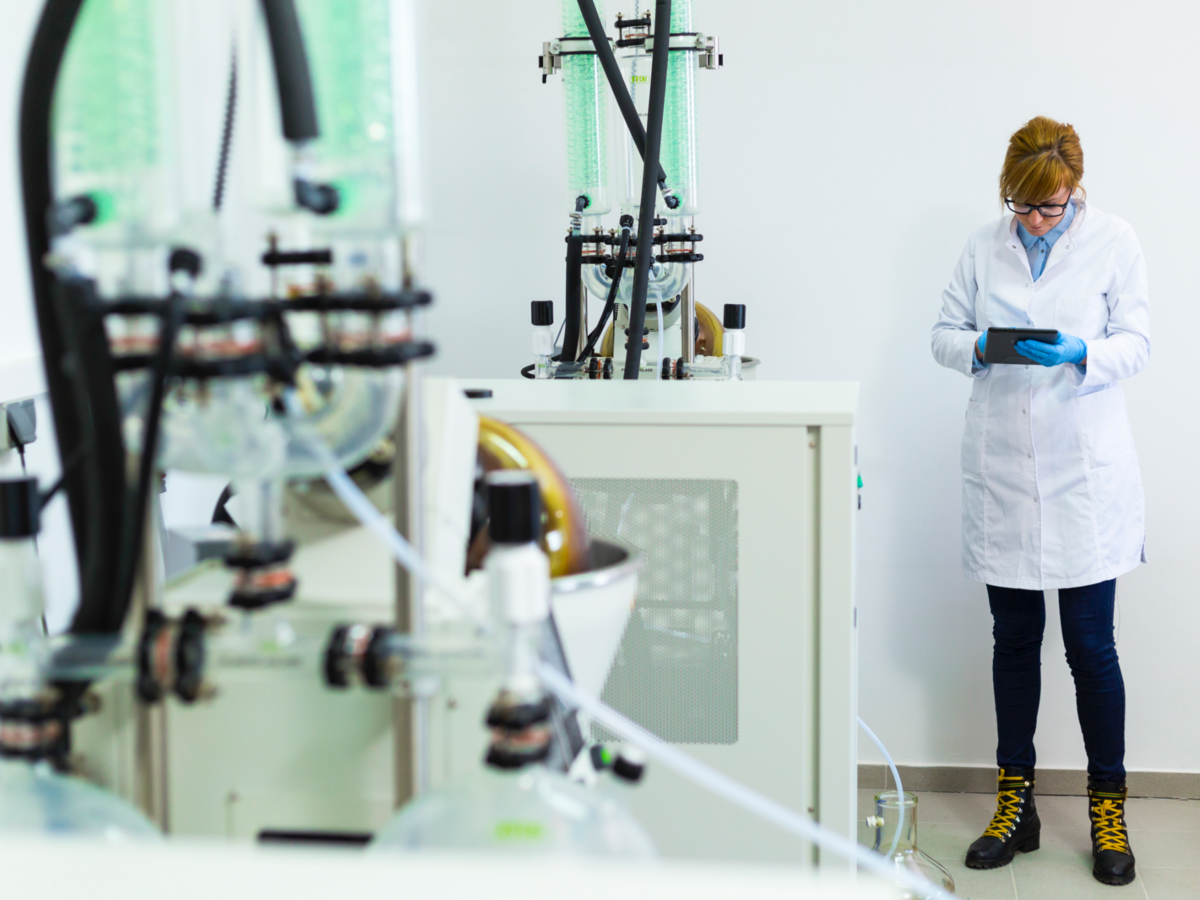 A scientist types on a tablet during CBDa oil extraction. She stands next to a rotational vaporizer.