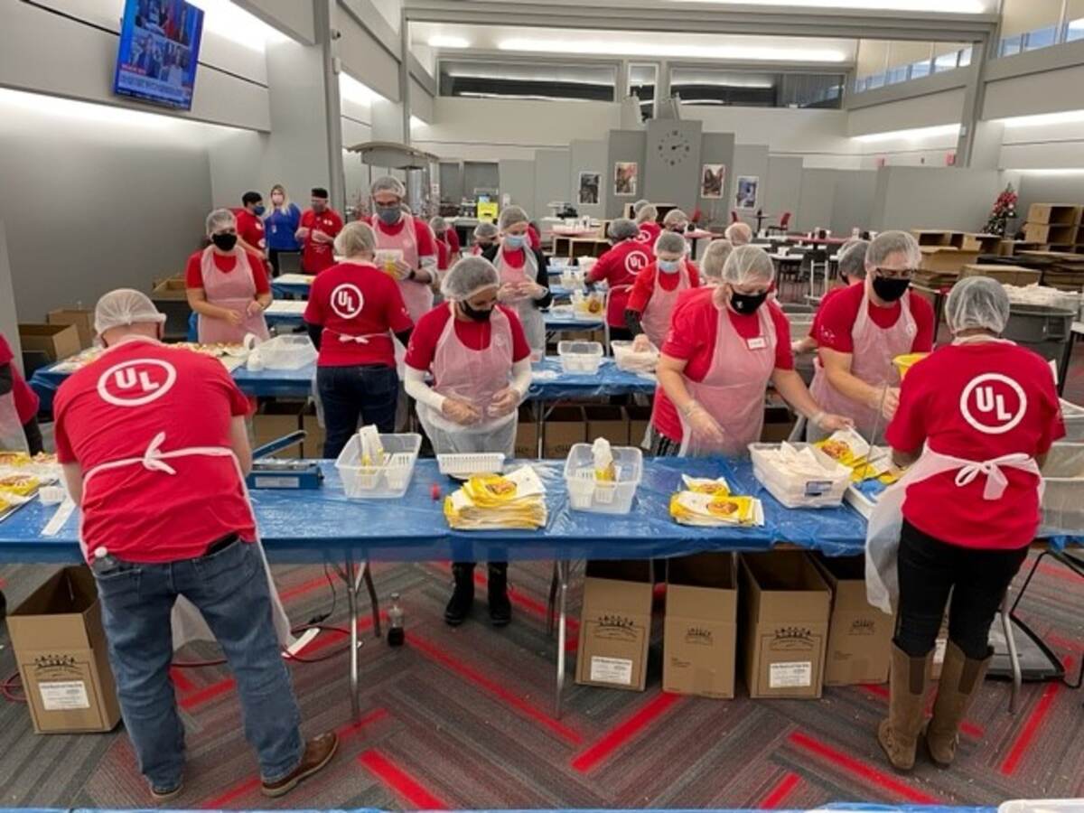 Wide shot of UL employees in red shirts packing meals for Impact 100. 