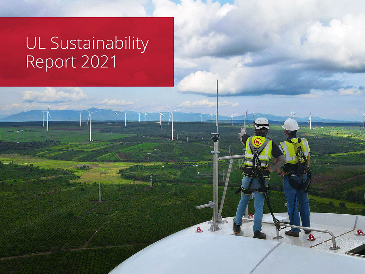 Two workers on top of a wind turbine overlooking a windfarm