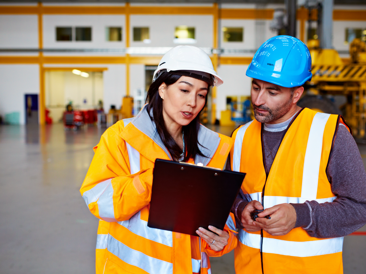 Two workers talking together over a clipboard while standing inside a large warehouse