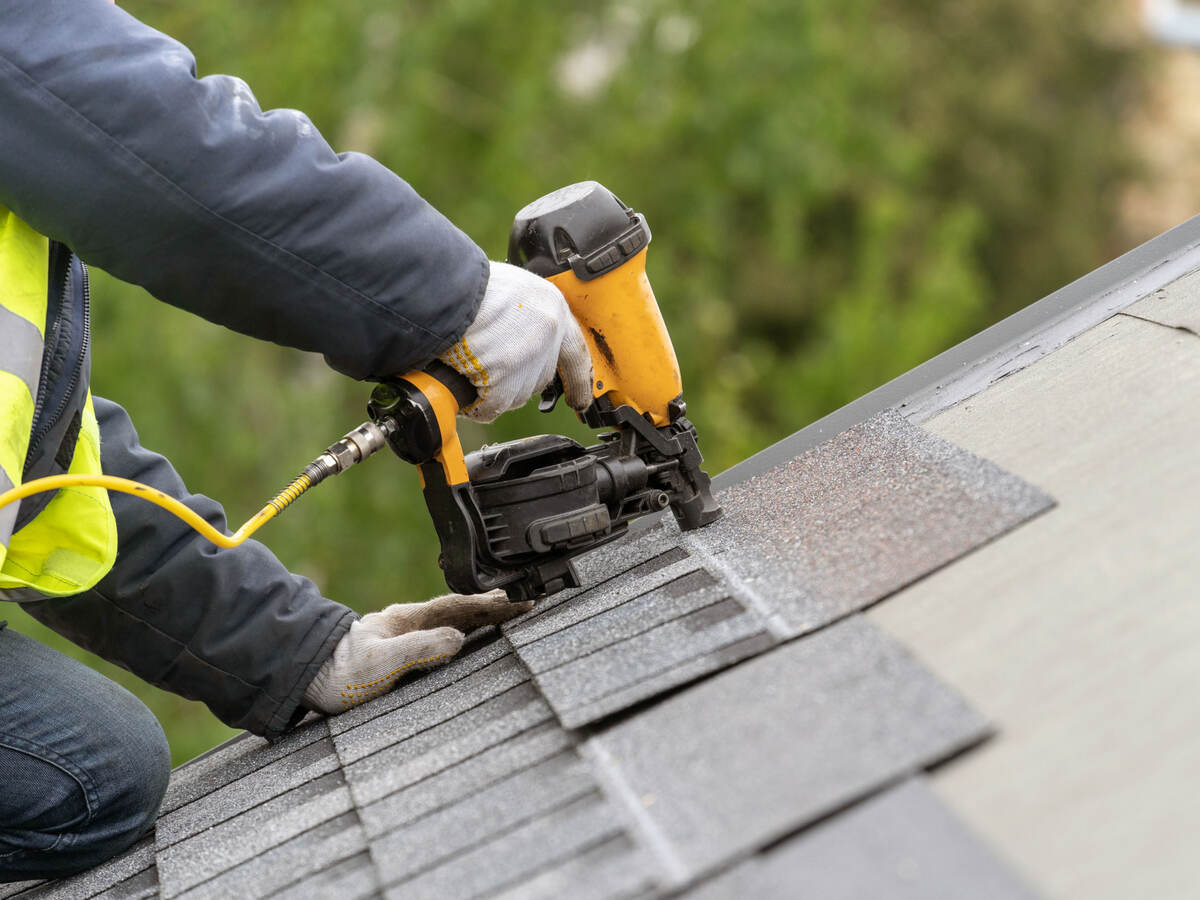Roofer using nail gun to attach shingles to a roof