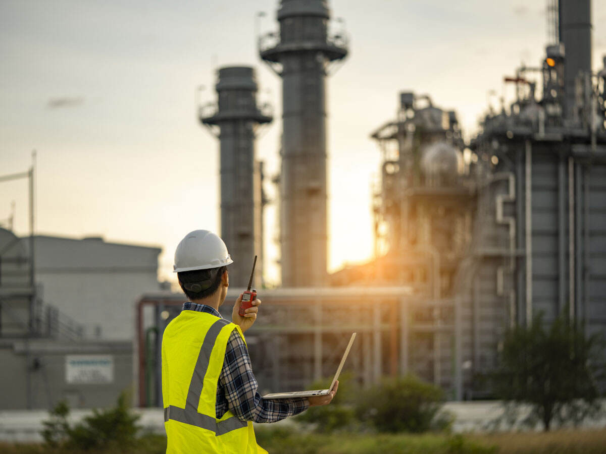 Engineer wearing a hard hat and safety vest working in gas turbine electric power plant at sunset