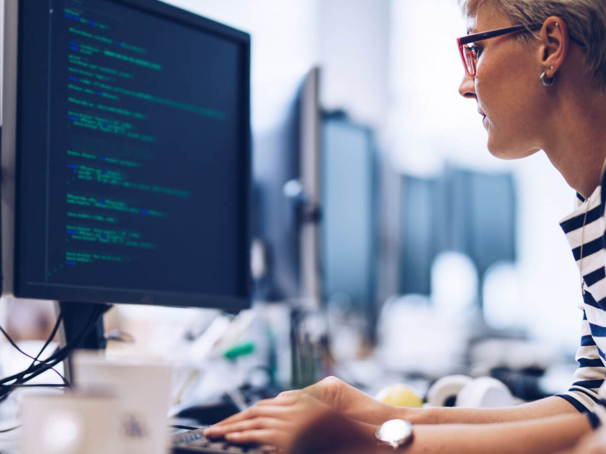 Programmer sitting at laptop and looking at a monitor