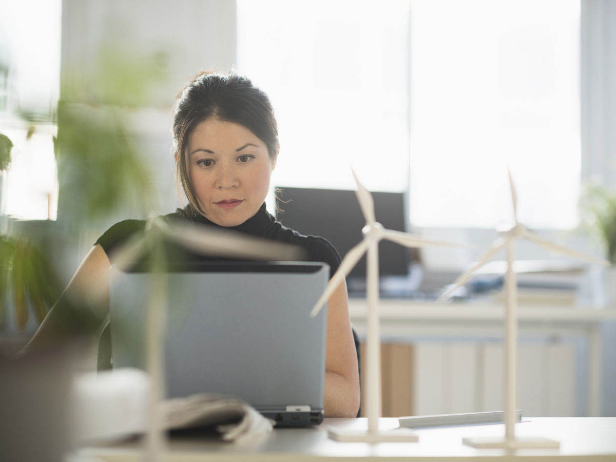 Person sitting at a desk using a laptop with miniature wind turbines sitting on the desk