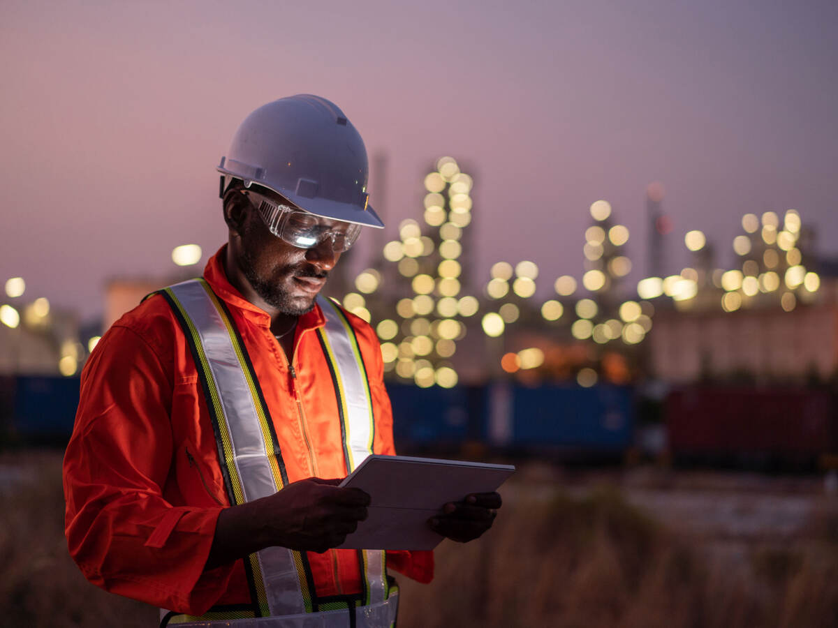 Engineer using tablet near an oil refinery at night
