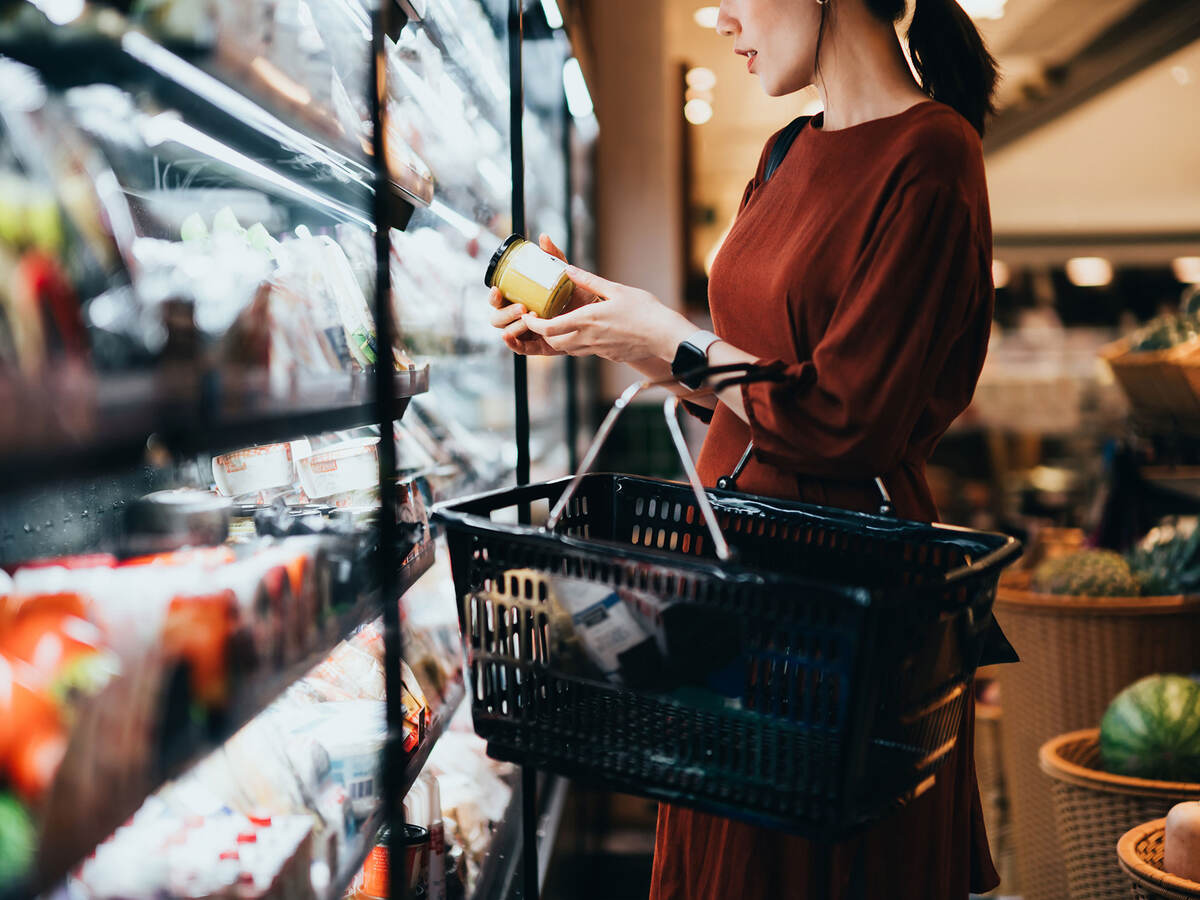 Cropped shot of young Asian woman carrying a shopping basket, standing along the dairy aisle, reading the nutrition label on the bottle of a fresh organic healthy yoghurt.