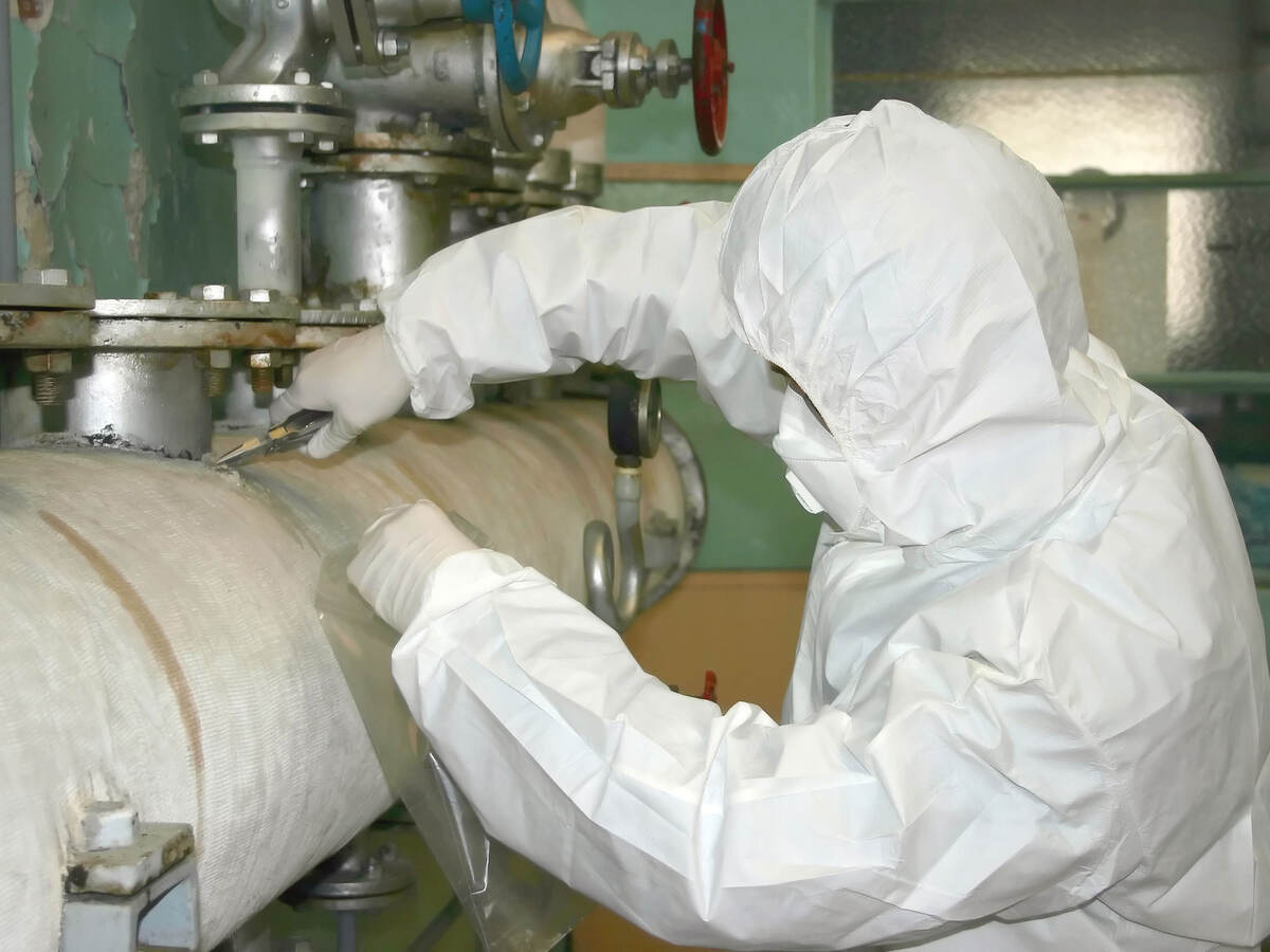 A worker wearing PPE and working with asbestos
