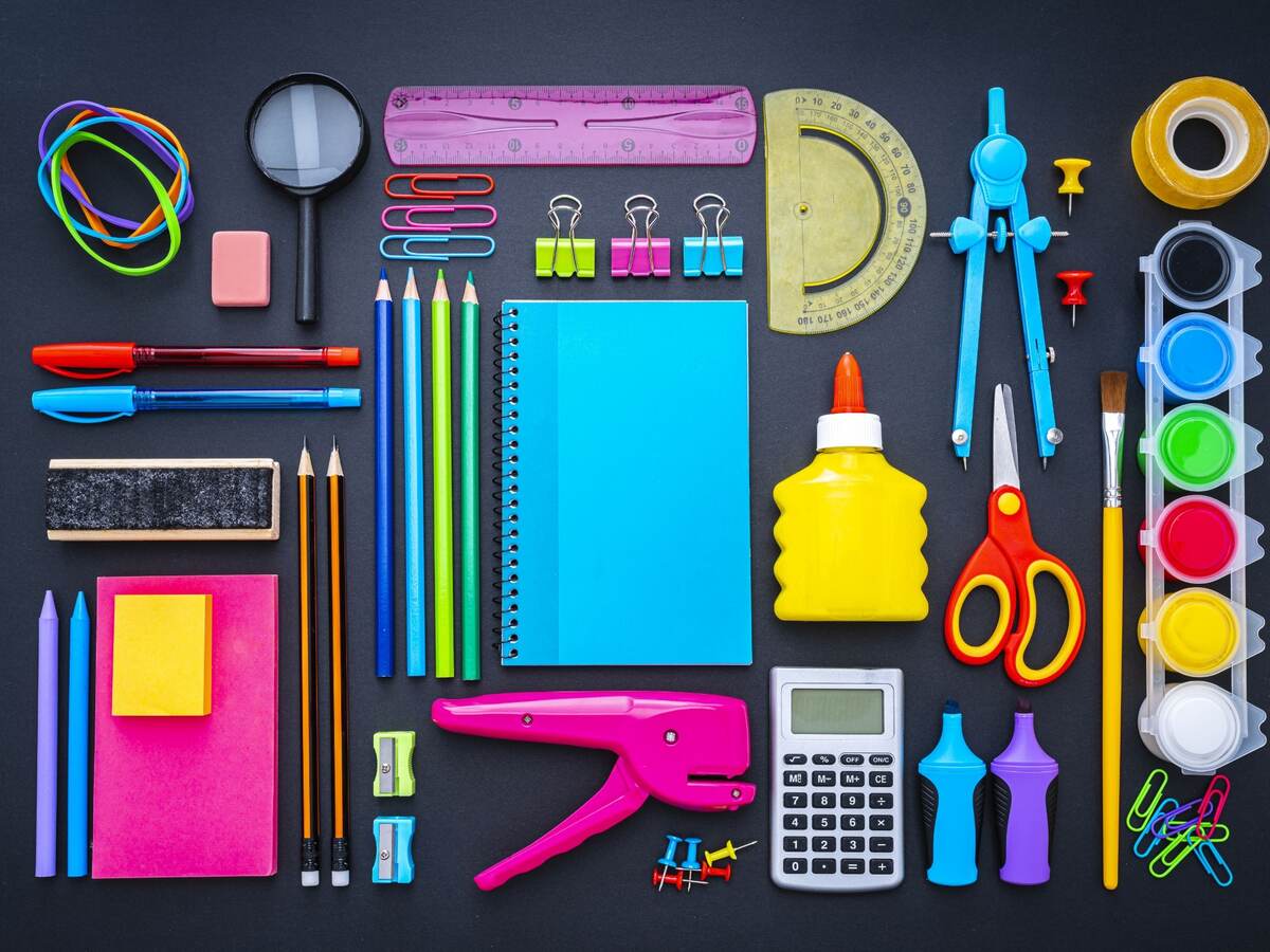 Forniture scolastiche multicolori girate dall'alto su sfondo nero.