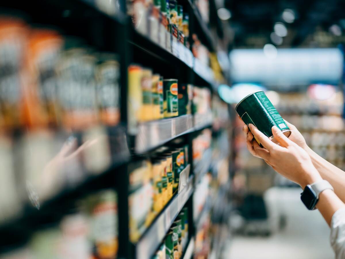 Close up of a woman grocery shopping in supermarket. Holding a tin can and reading the nutrition label at the back.