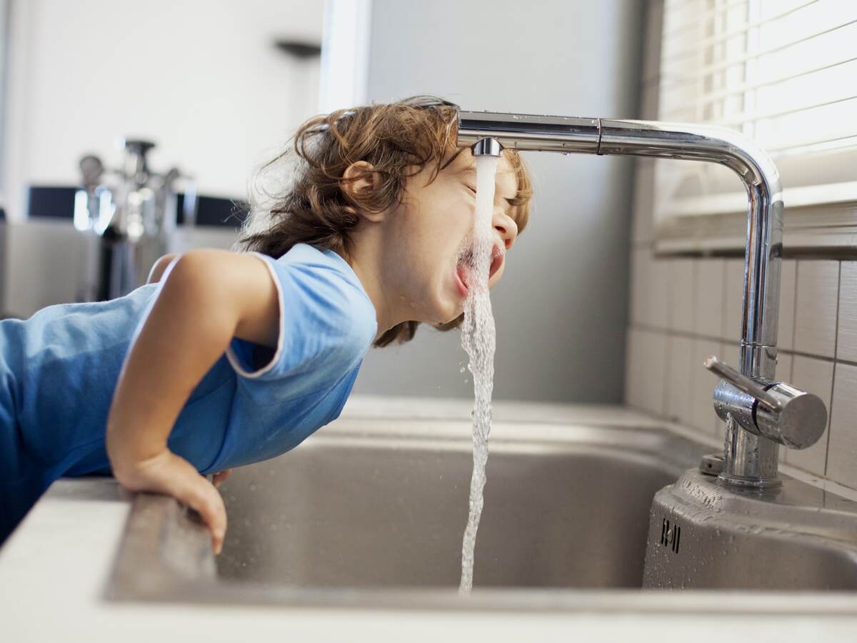 Small boy drinking water out of faucet.