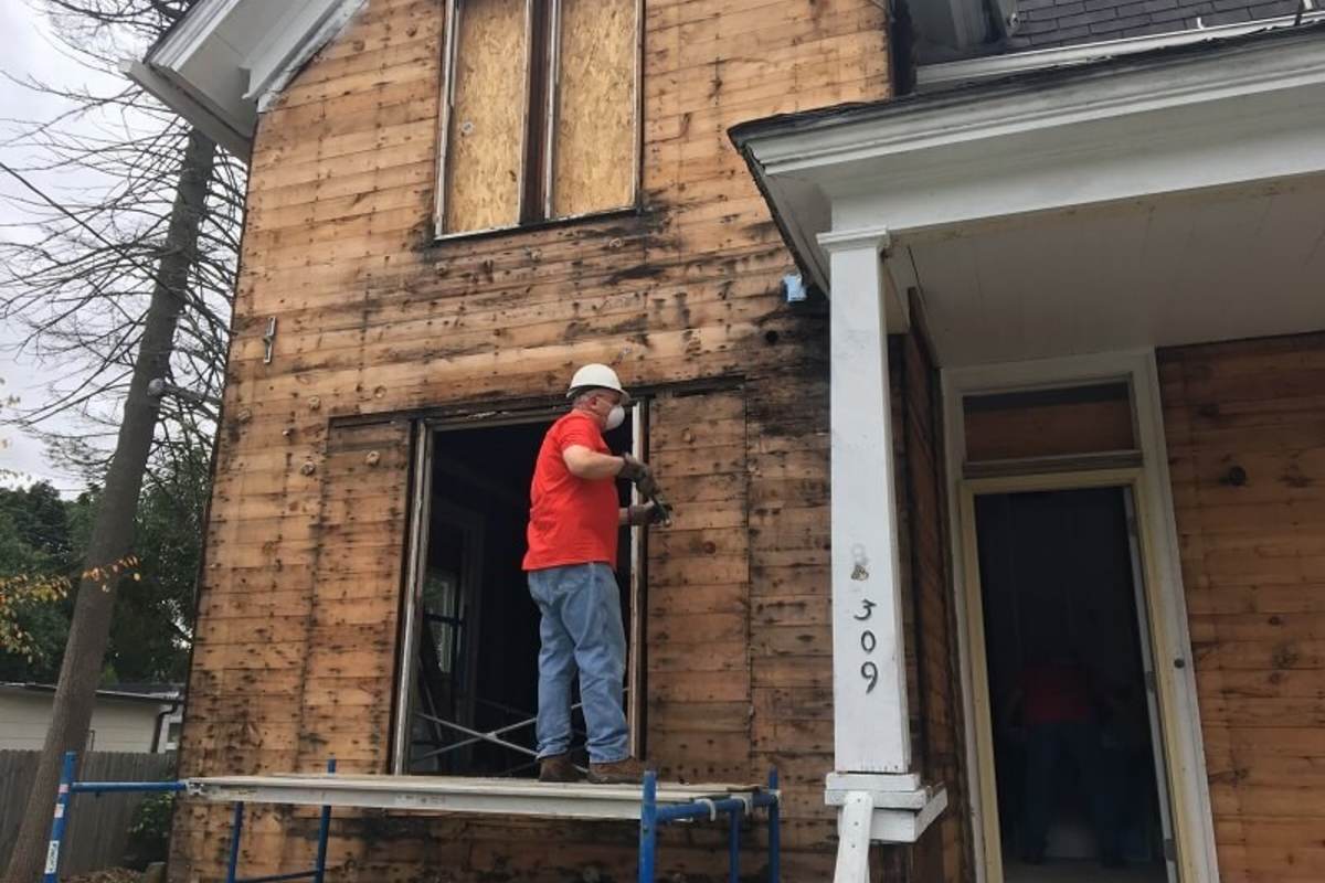 A UL volunteer stands on scaffolding, measuring an opening for a new window