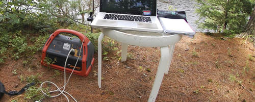 Portable power pack connected to laptop in a nature scene.