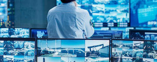 Person standing in a control room looking at security video feeds